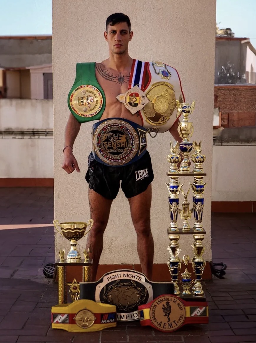 Marc Dass Rey posando con sus cinturones y trofeos de Muay Thai
